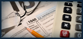 Image of different tax documents with a pencil, calculator and glasses laying over them.